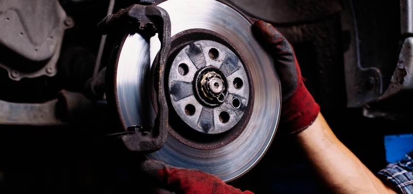A man holds a brake disc while inspecting a car's braking system