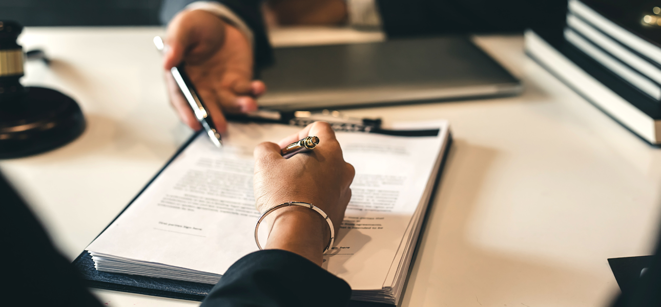 A business person in a suit signing a contract on a desk with a pen