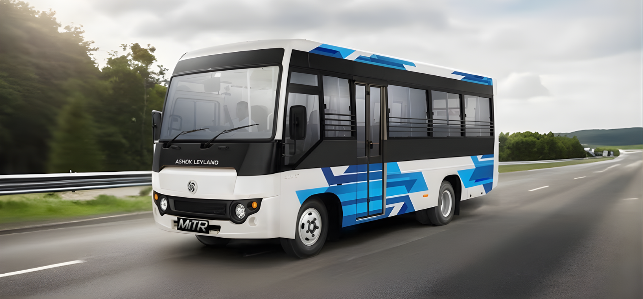 An Ashok Leyland MITR bus travels down a road with trees and mountains in the background