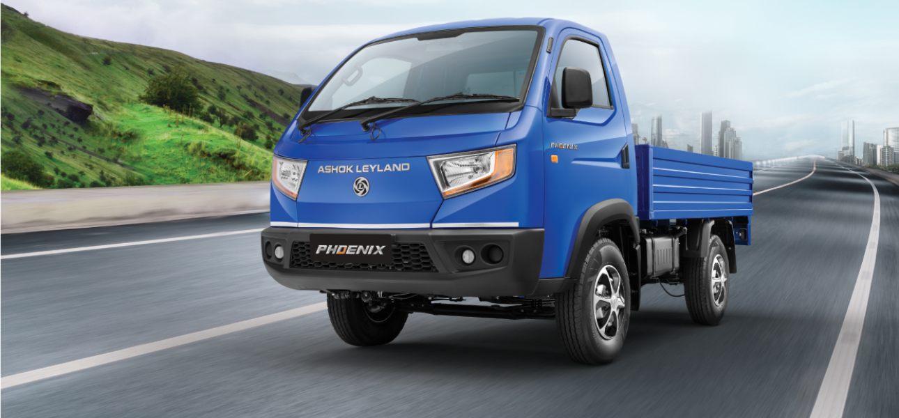 An Ashok Leyland Phoenix truck driving down a road surrounded by greenery.