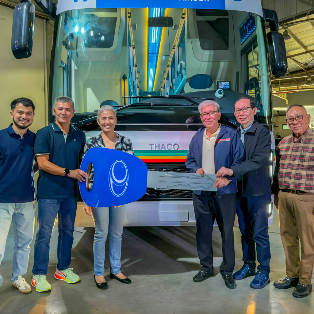 A group of people stands together in front of a bus, smiling and chatting.