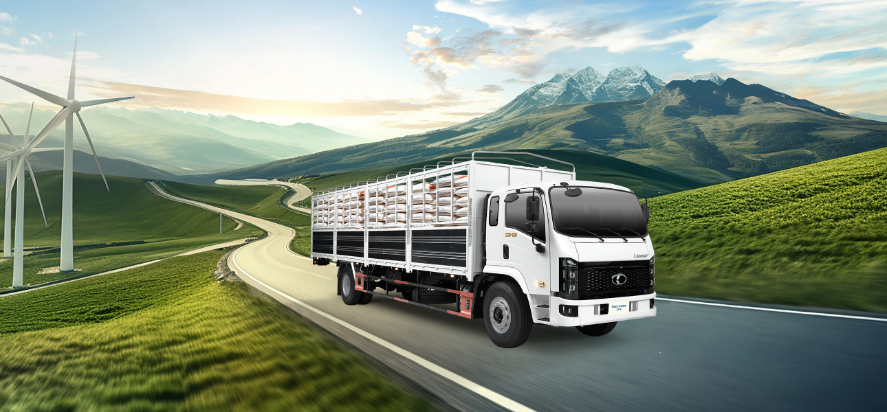 A Linker T2-16 drives along a road with several wind turbines visible in the background against a clear blue sky.