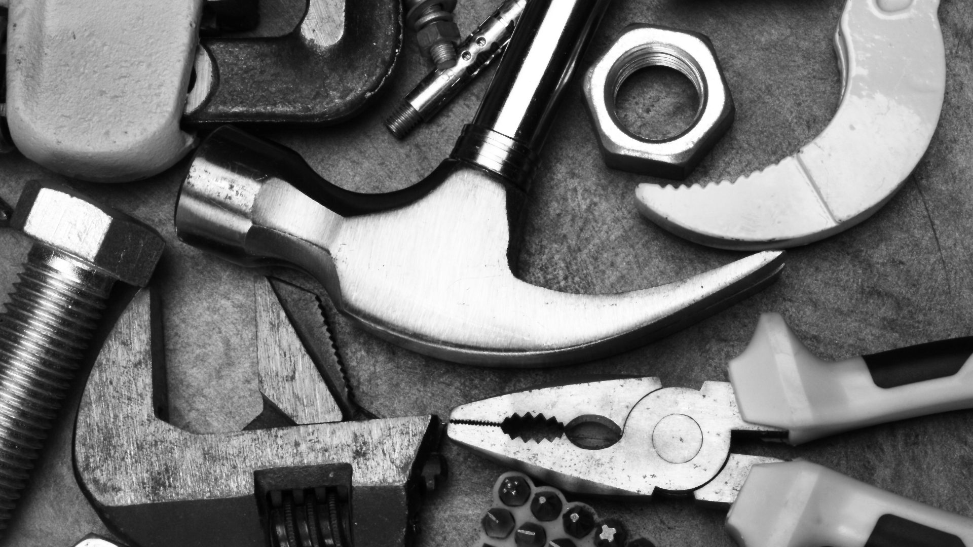 Black and white image of assorted tools including a hammer, pliers, wrench, and bolts.
