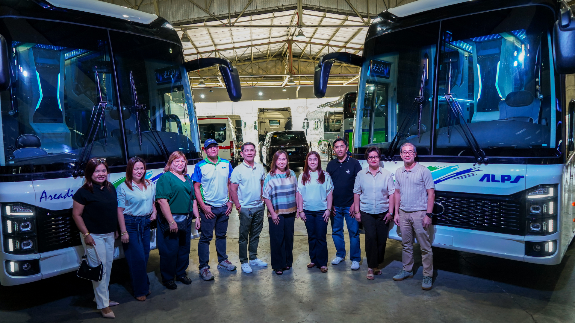 A group of ten people standing in front of two large, modern buses inside a well-lit depot.